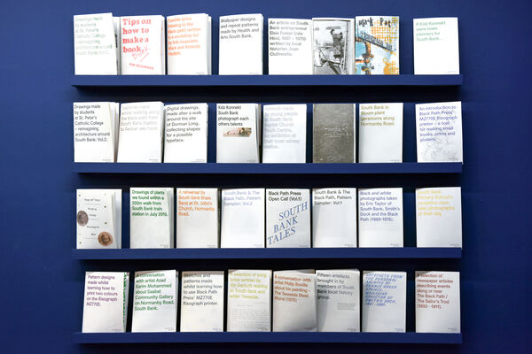 A series of risograph zines displayed on a dark blue wall.
