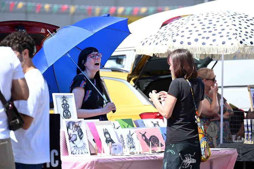 Lady at booth talking happily with visitor who is interested in her drawings.