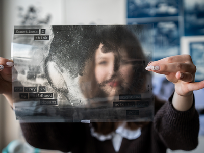 Person holding up a black and white photo print up over their face.
