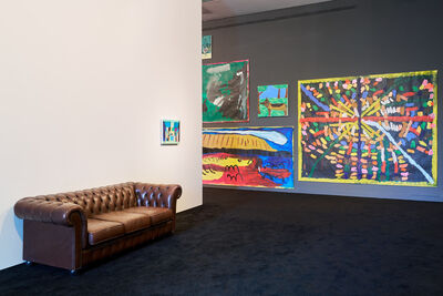 Room with dark grey carpet, a brown leather sofa against one wall and colourful abstract paintings on the right.