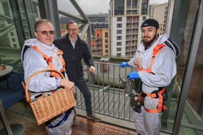 Two bee keepers and a man stand on Baltic rooftop