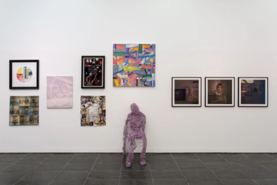 A pink figure sits in front of a wall covered in artworks