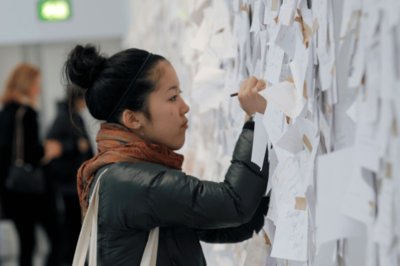 A woman writing on paper hung up on a wall