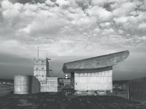 Black and white photo of a brutalist building under a cloudy sky.