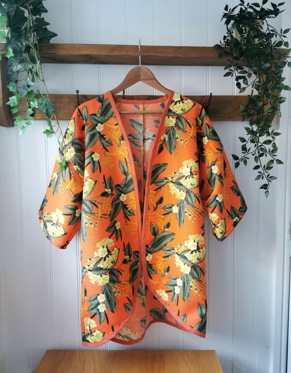 An orange kimono-style jacket with a blossoming flower pattern hangs on a shelf.
