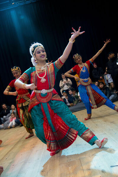 Woman wearing colourful red and teal clothes and head dress, dancing.