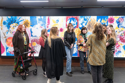 Group of people stood together in front of a large colourful artwork.