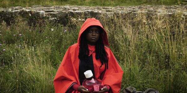 Person sat in grassland wearing a red hooded jacket. 