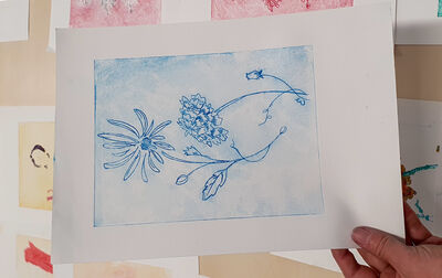 A hand holds a print of two blue flowers on white paper