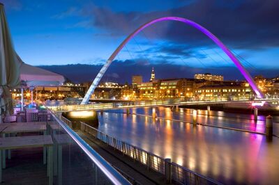 Evening photo of a river with bridge lit up in purple.
