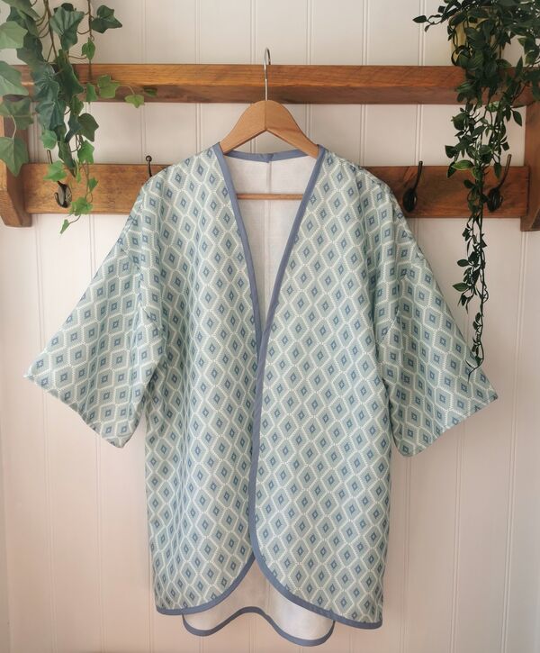 A blue kimono style jacket with a diamond pattern hands from a wooden shelf.