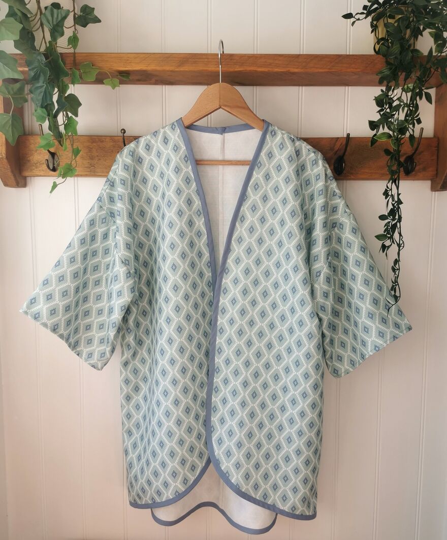 A blue kimono style jacket with a diamond pattern hands from a wooden shelf.