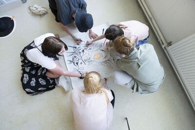 Group of young people drawing together whilst on the floor. 