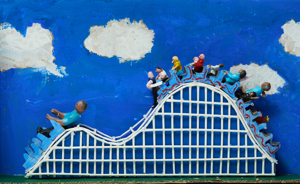 A clay sculpture of people on a rollercoaster against a blue sky with fluffy white clouds.
