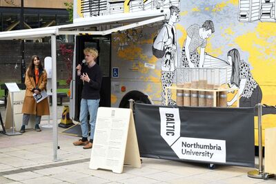 Person speaking into microphone with Baltic x Northumbria University signage