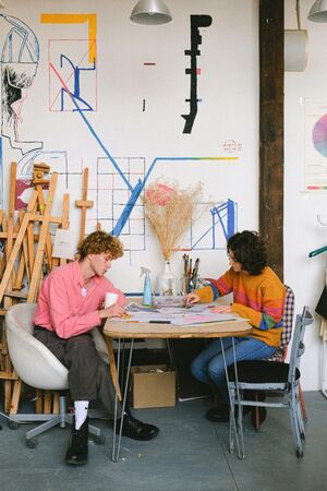 Two people sat at a wooden desk sketching and painting.