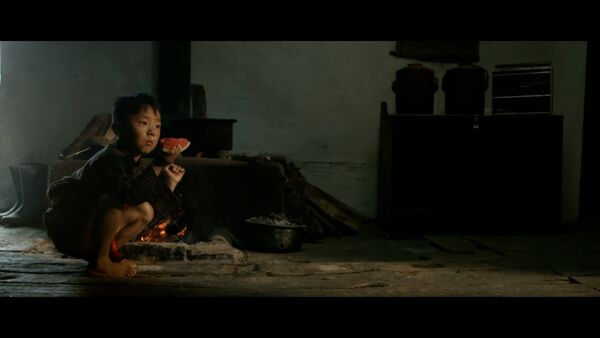 Small boy wearing black squatting in front of a fire and holding a melon.