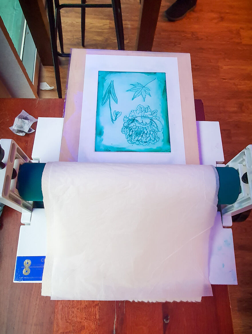 A blue etching of a flower set up on a printing machine.