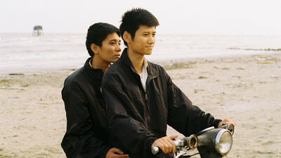Two vietnamese men on a motorbike together on a beach.
