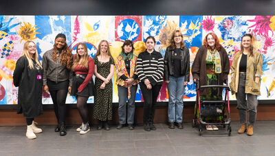 Group of nine young people stood in a line against a colourful wall.