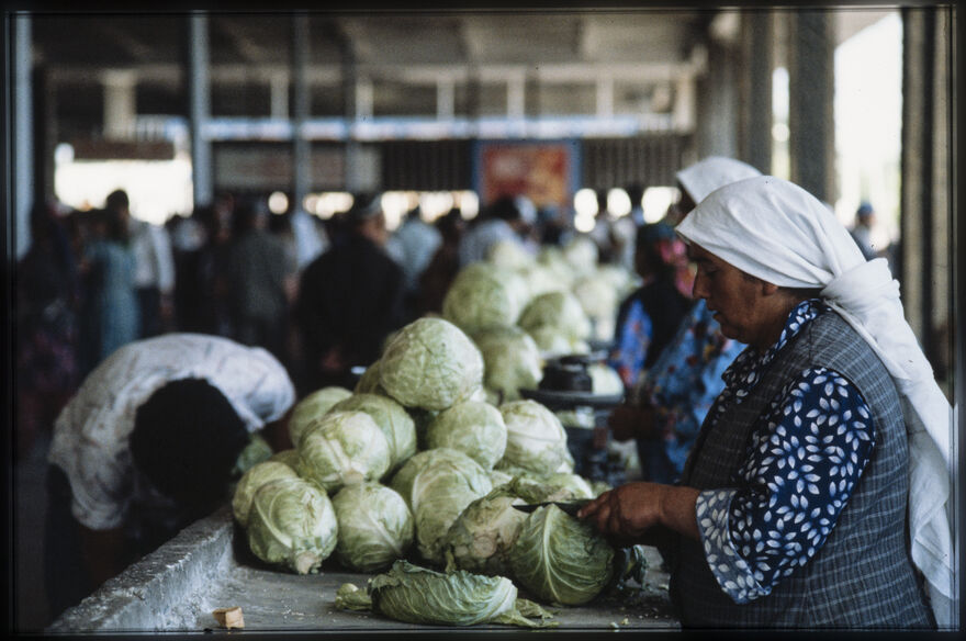 Woman wearing a head scarf and blue shirt chopping lettuce.