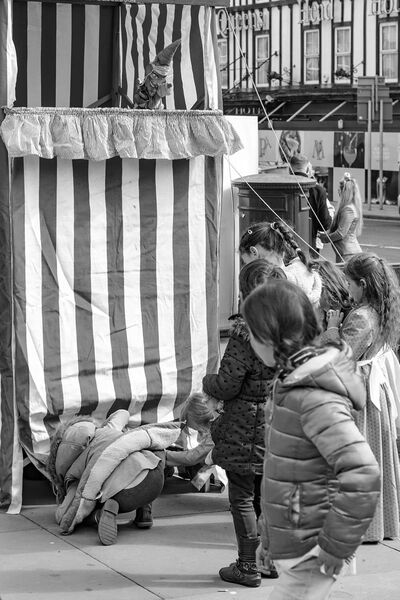 A group of children looking at a Punch and Judy tent. One child peeks under the tent.