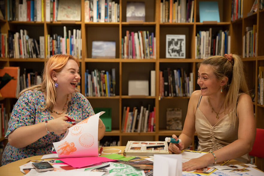 Two people laugh over the zines they are making.