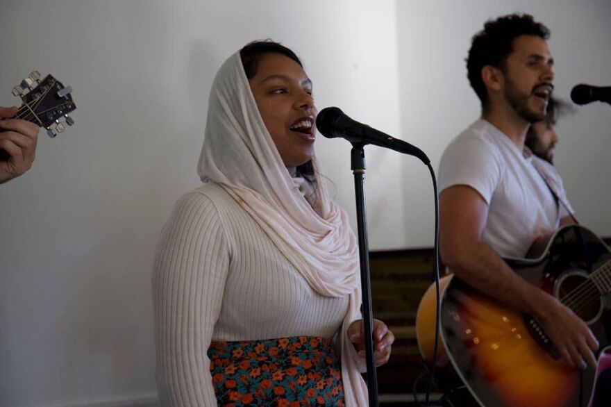 A woman singing into a standing microphone next to a man playing a guitar