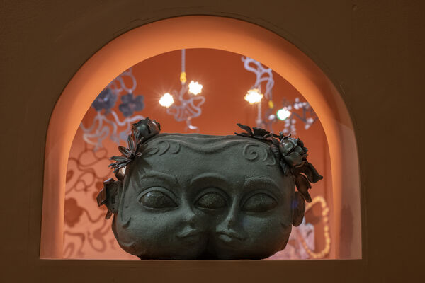 A sculpture of two conjoined heads resting on a shelf in an orange archway.