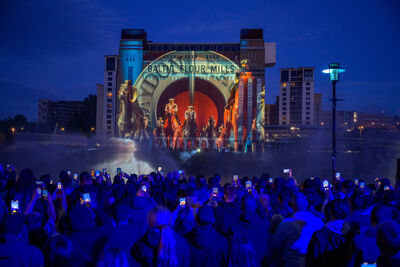 Large projection of the blaydon races on the side of Baltic's building with a large crowd of people stood warching.