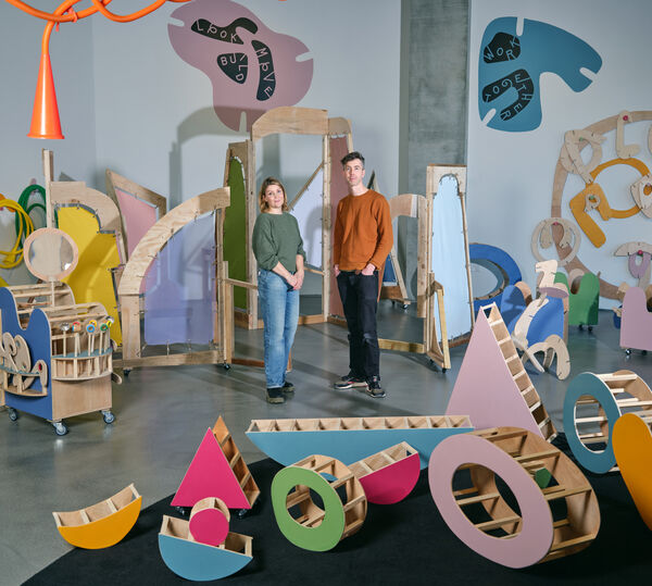 Two artists stand amongst colourful sculptures 