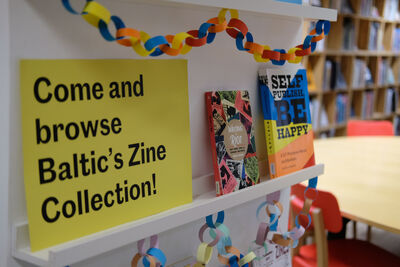 Shelf with books and a yellow sign that says 'Come and browse Baltic's Zine Collection!'