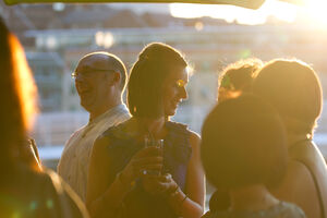 People stood smiling and chatting, holding drinks and lit up gold by the sunset.
