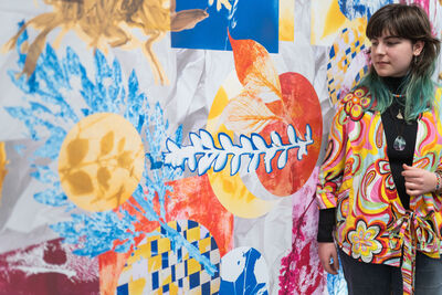 Person wearing a colourful shirt stood against a colourful wall.