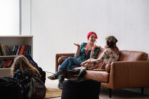 Two young people sat on a brown leather sofa talking animatedly.