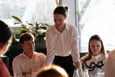 Woman wearing a white shirt smiling and placing plates of food on a table for people.
