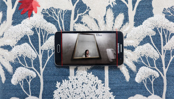 A Samsung phone displaying a photo of a person reflected in an ornate gold mirror.