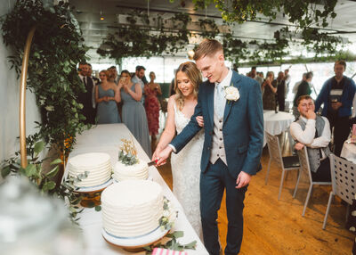 Two people wearing wedding attire smiling and cutting a cake.