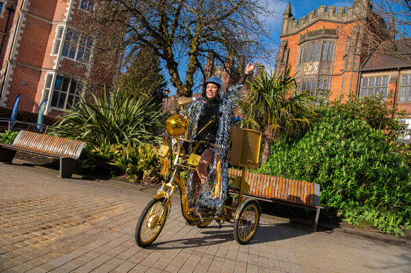 A golden trycycle in the middle of a path with a person riding it and smiling.