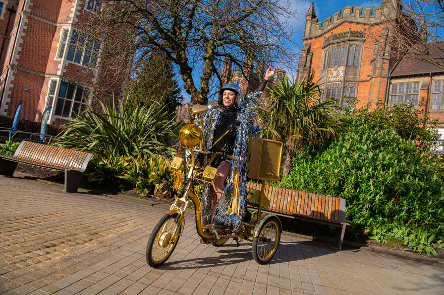 A golden trycycle in the middle of a path with a person riding it and smiling.