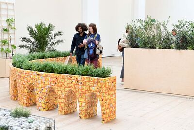 Two people look at a curved, l-shaped plant pot in the exhibition.