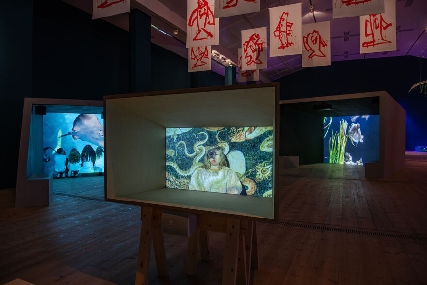 A dark room with three large screens in containers showing films about marine ecology.
