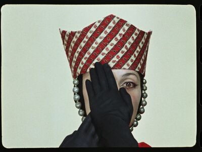 Woman wearing a red and white hat and black gloves holding her hands over her face.
