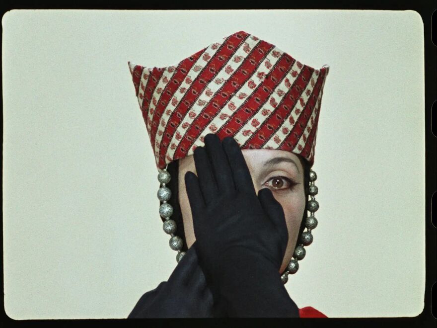 Woman wearing a red and white hat and black gloves holding her hands over her face.