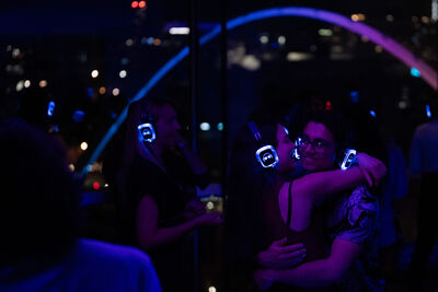 People dancing and hugging wearing light-up headphones with a view of the Quayside in the background