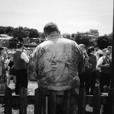 A person in a dirty worker's jacket overlooks a crowd of people.