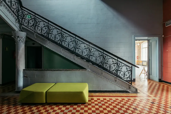 Hallway with ornate black railed staircase and yellow and red checked tiles.
