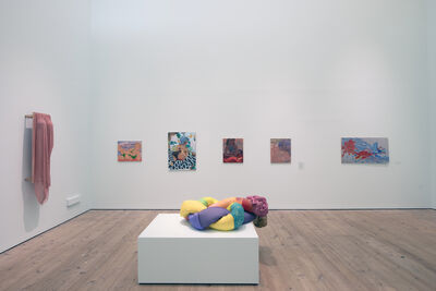 A white room with five canvas paintings and a pink silk dress displayed on the walls. In the middle of the space there is a sculptural installation of a colourful fabric tube tied in a knot with expanding foam leaking out both ends.