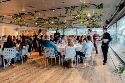 Room of people sat at tables smiling, talking and being served dinner.