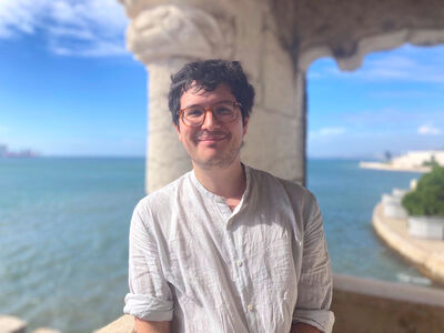 Person with glasses smiling with waterfront behind. 